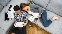 A couple review a list of items while relaxing on their grey couch.